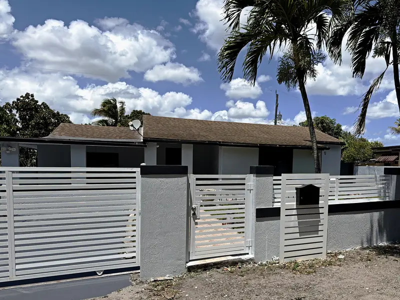 Single-story stucco home in the Miami area after exterior painting, stucco repair and wall refinishing by Greenbelt crews: gray walls with dark trim
