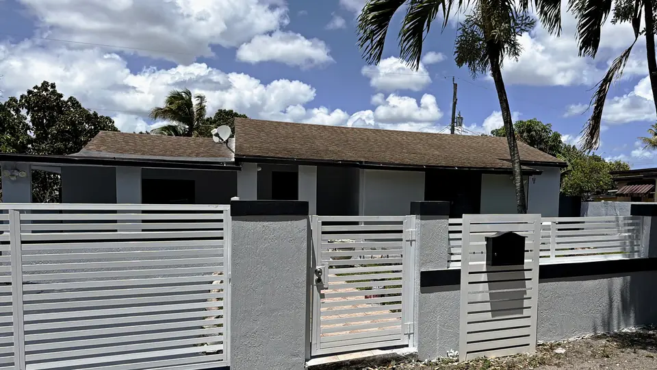 Single-story stucco home in the Miami area after exterior painting, stucco repair and wall refinishing by Greenbelt crews: gray walls with dark trim